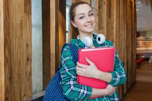 Girl holding book standing in school hallways.
